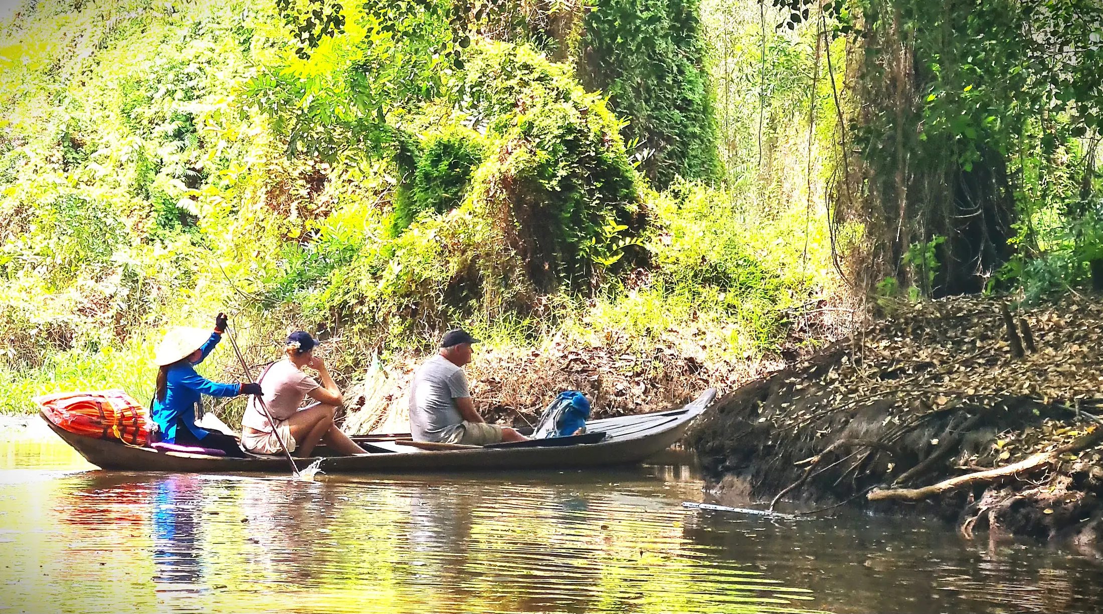 A small boat carrying visitors through a shaded natural canal